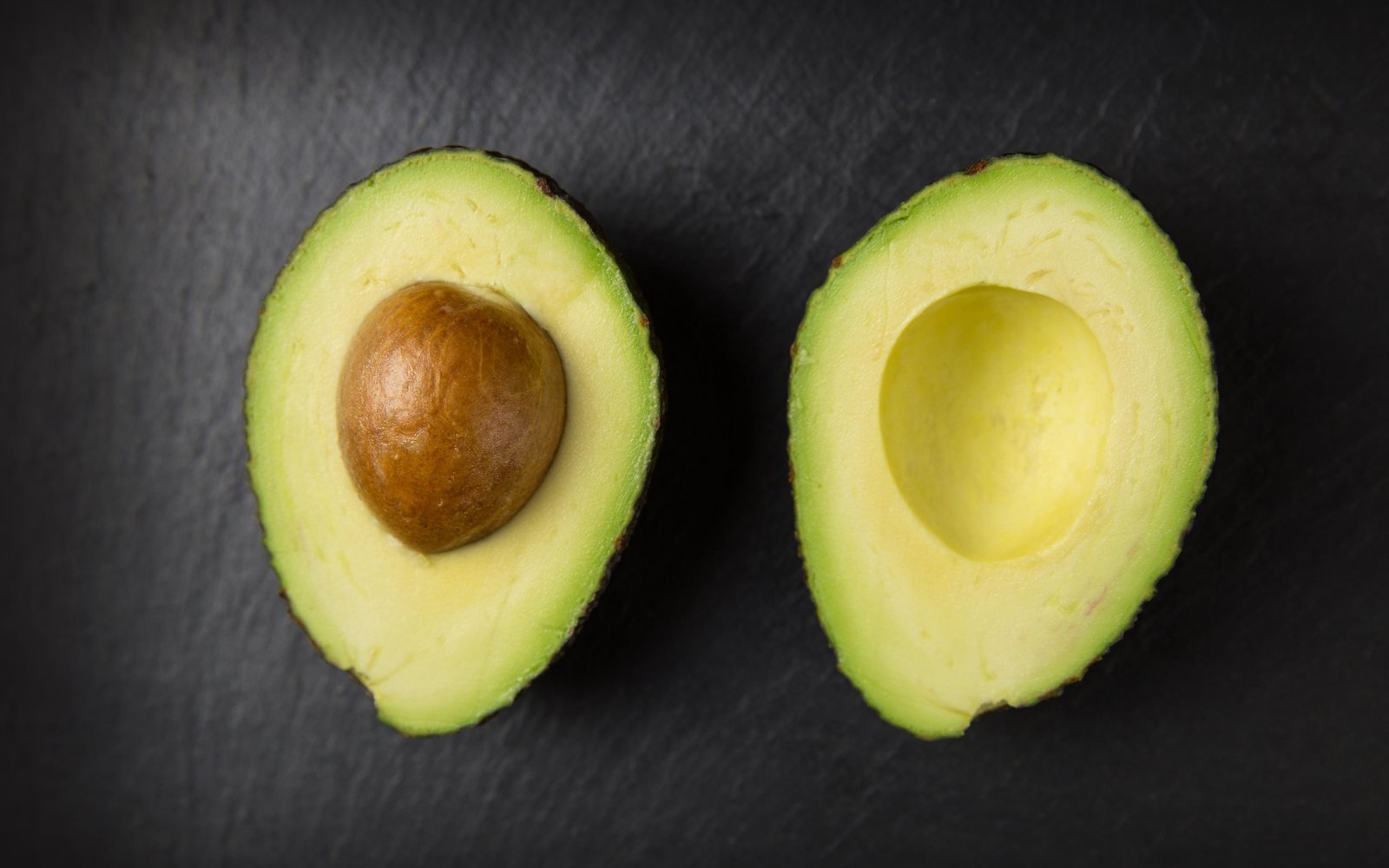 Halved avocado on a dark surface for portion guidance