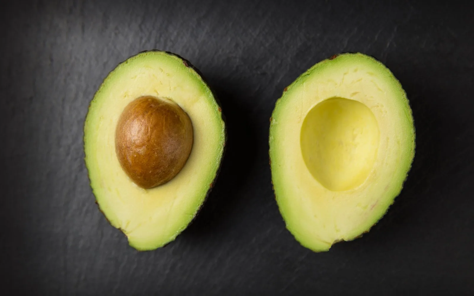 Halved avocado on a dark surface for portion guidance
